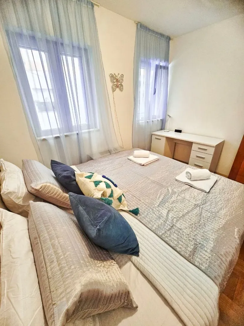 A furnished bedroom with a double bed, desk, and windows.
