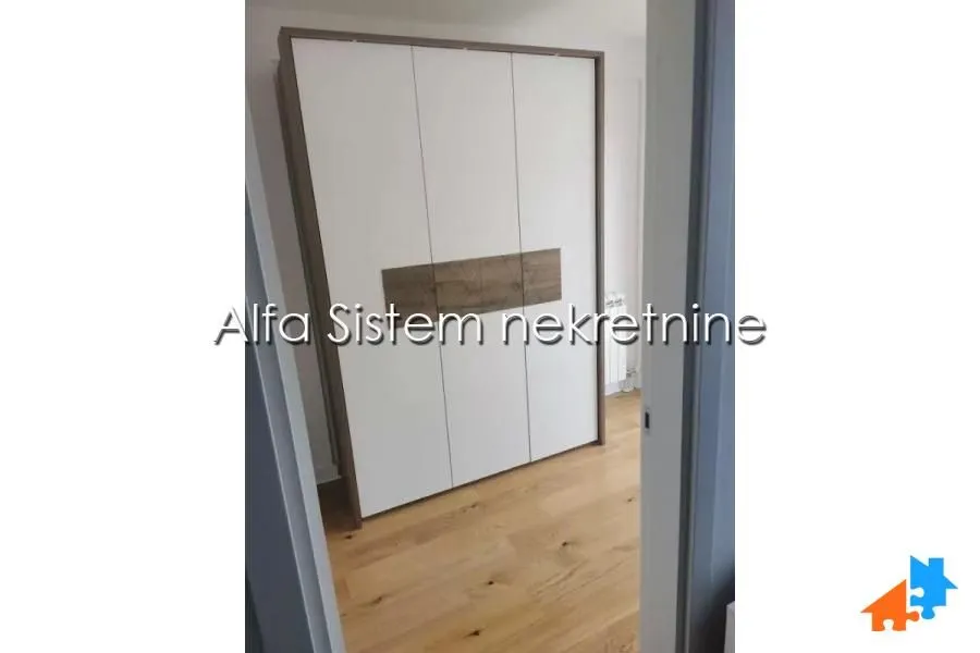 Pogled na spavaću sobu sa ugradnim plakarom i drvenim podom kroz vrata.