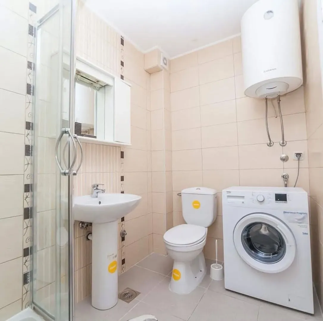 Compact bathroom with a shower cabin, sink, toilet, and washing machine.