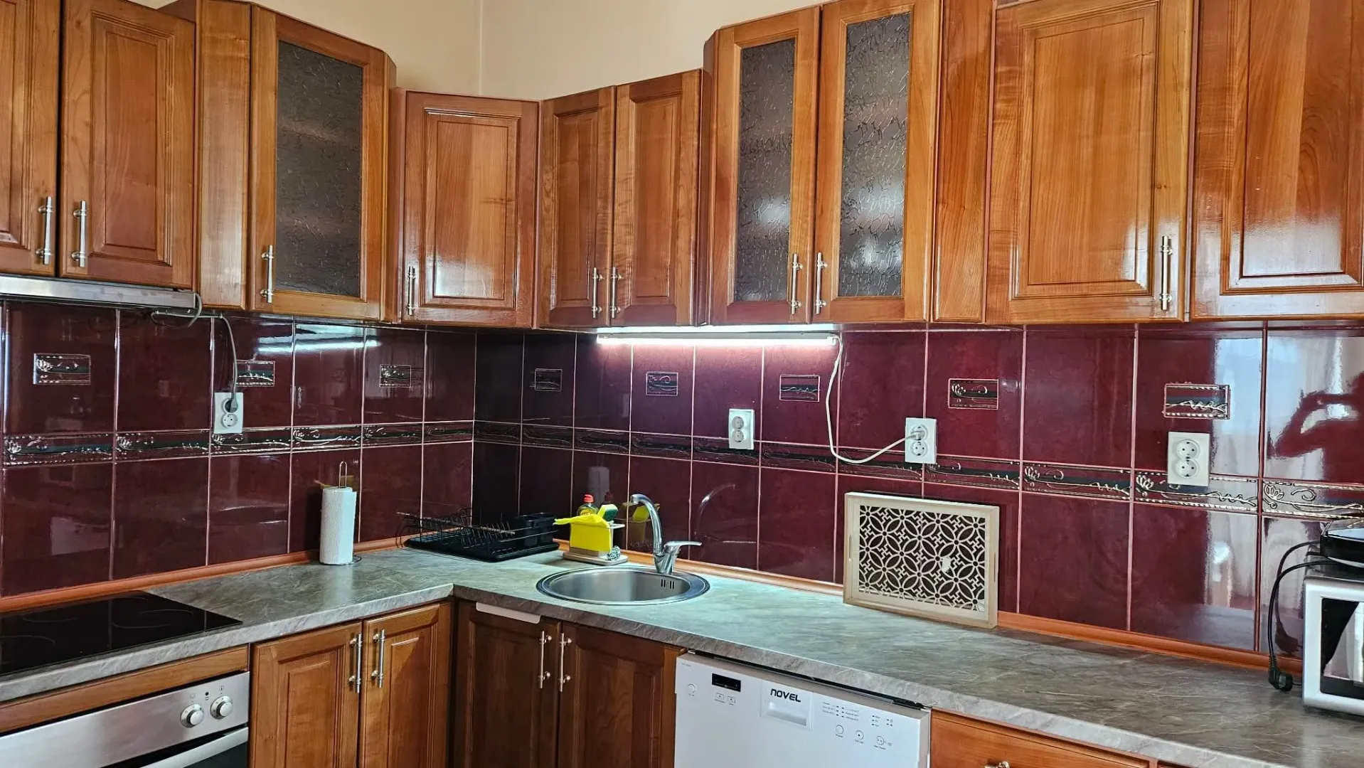 Wooden kitchen with dark countertops and red wall tiles.