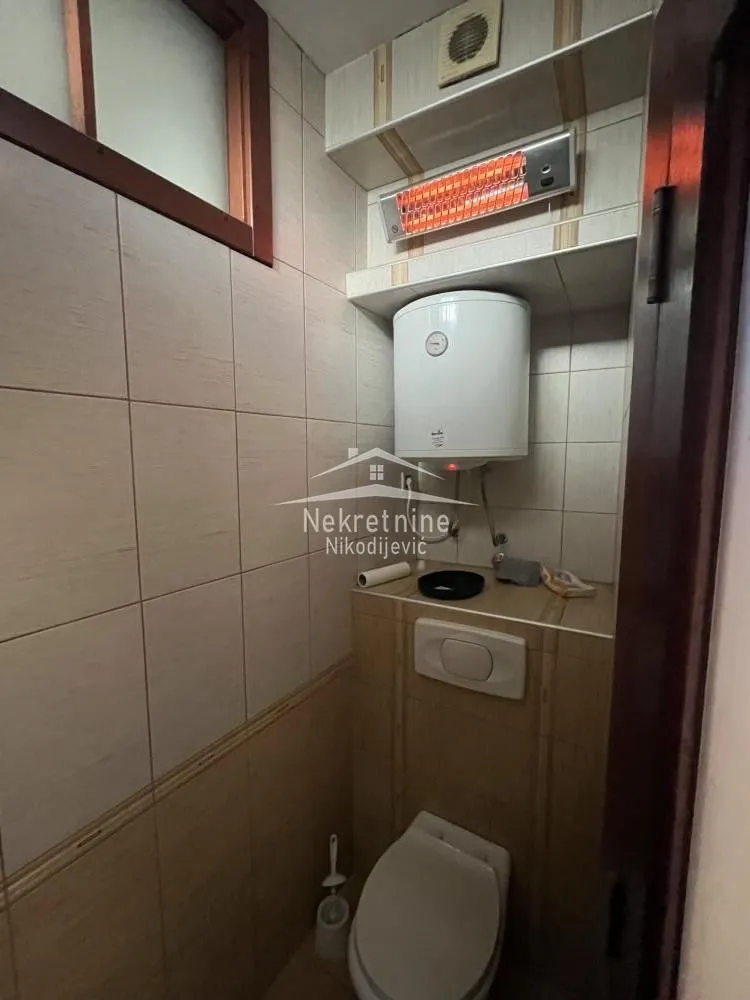 Smaller bathroom with a toilet, water heater, and wall heater.
