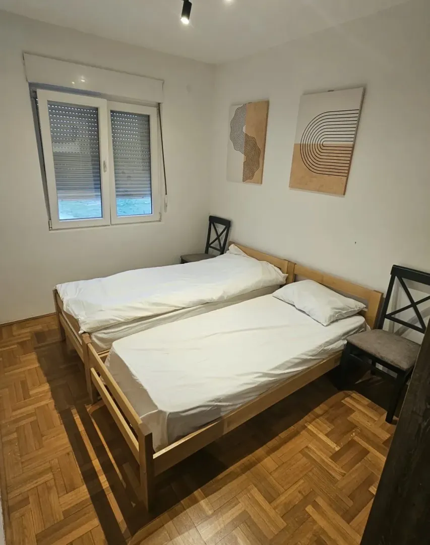 Spavaća soba sa dva kreveta na spajanje i parketom na podu.