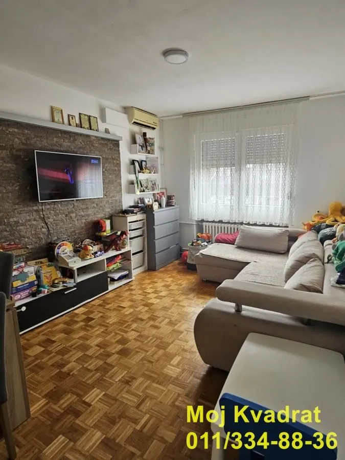 Dnevna soba sa garniturom za sedenje, televizorom i parketom na podu.