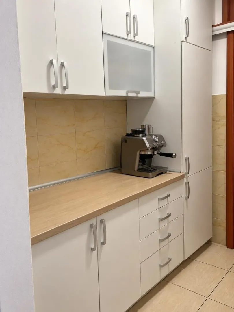 Bijeli kuhinjski elementi sa radnom površinom u boji drveta i aparatom za kafu.