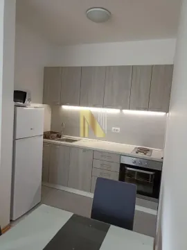 Manja opremljena kuhinja sa belom tehnikom i trpezarijskim stolom u prvom planu. - image 3