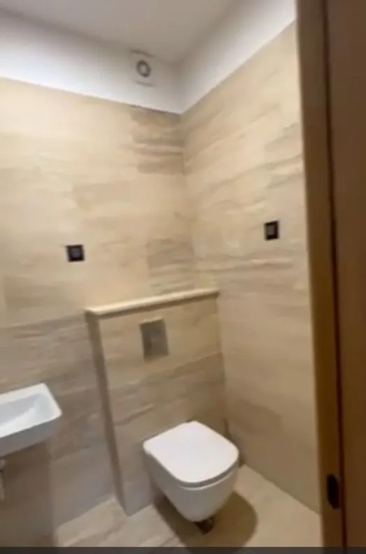 Moderno kupatilo sa bež pločicama i visećom wc šoljom.