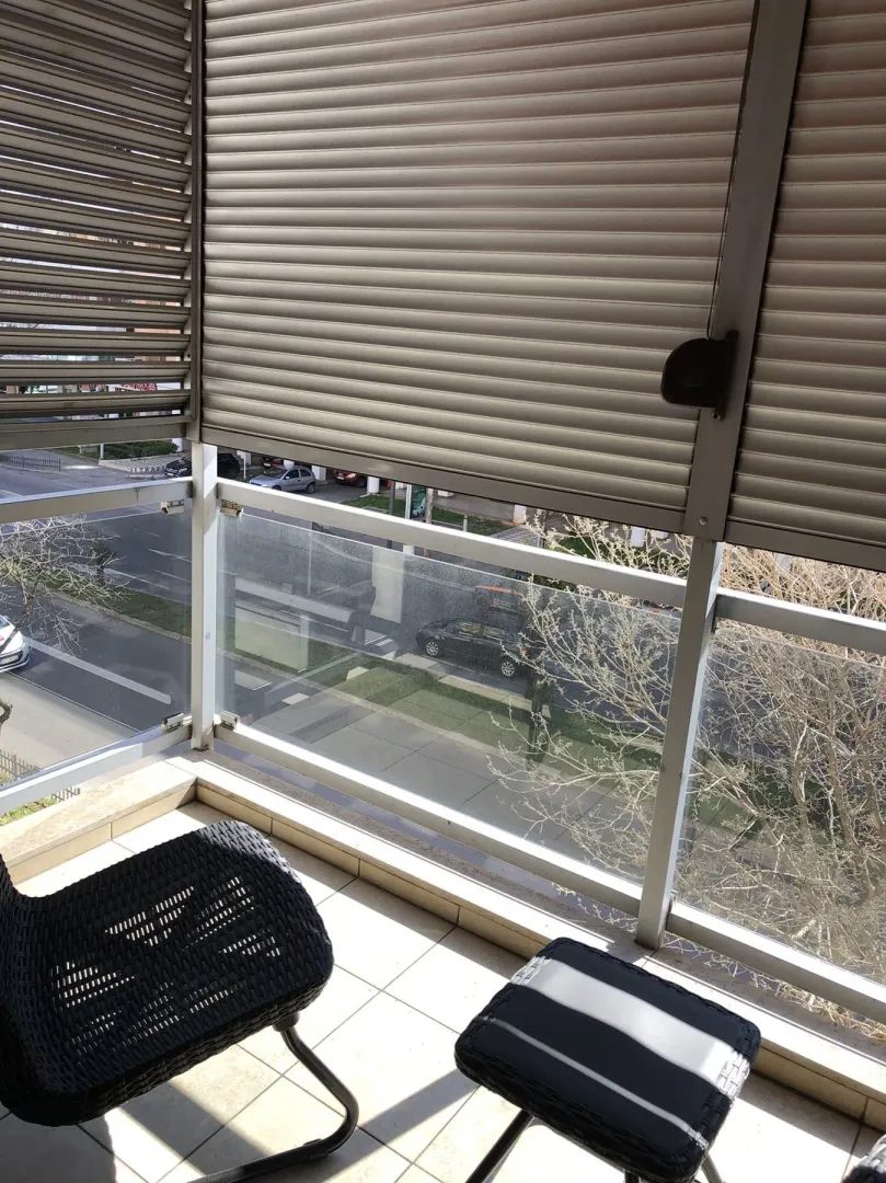 A balcony with a glass railing, shutters, and a view of the street.