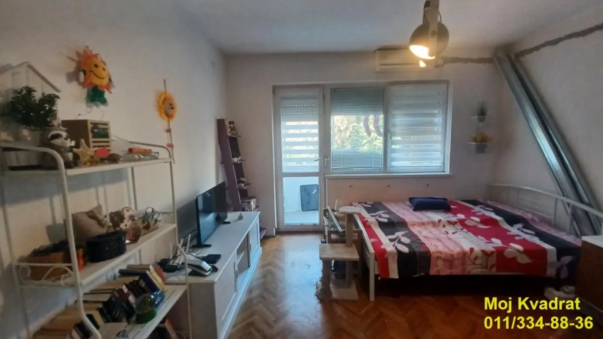 Nameštena spavaća soba sa krevetom, TV komodom i izlazom na terasu.