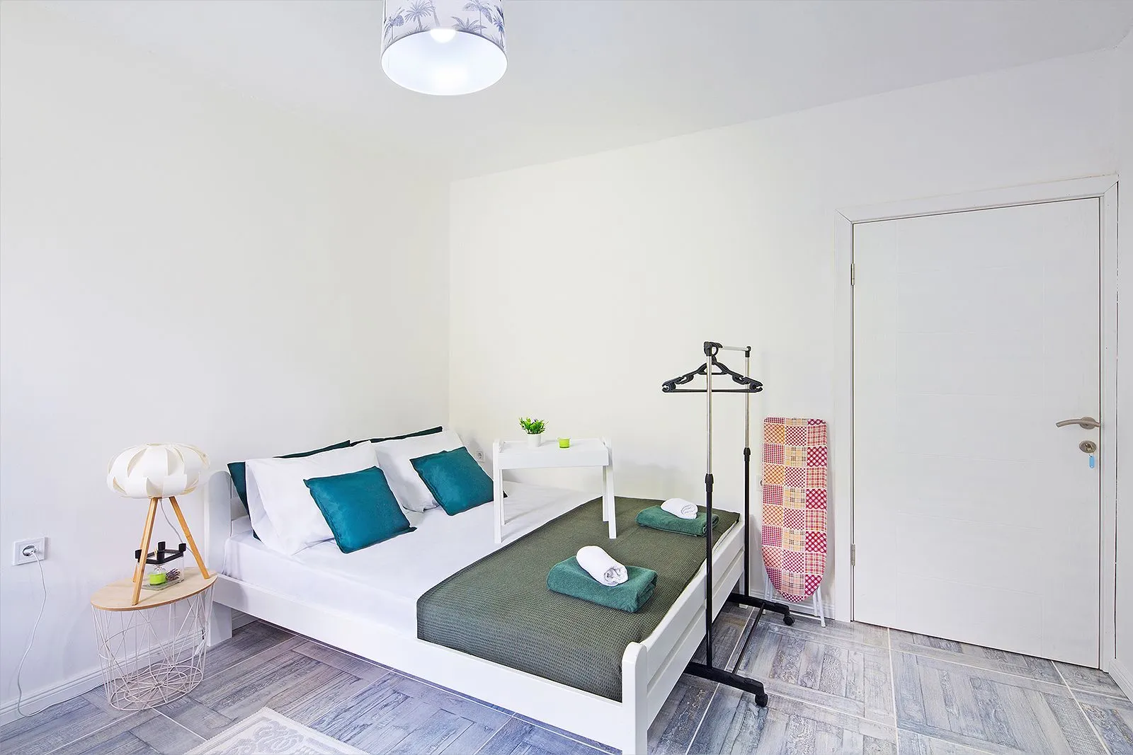 Furnished bedroom with a double bed, white walls, and tiled flooring.