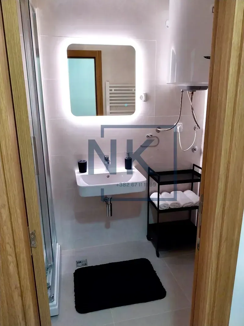 Smaller bathroom with a shower cabin, washbasin, and backlit mirror.