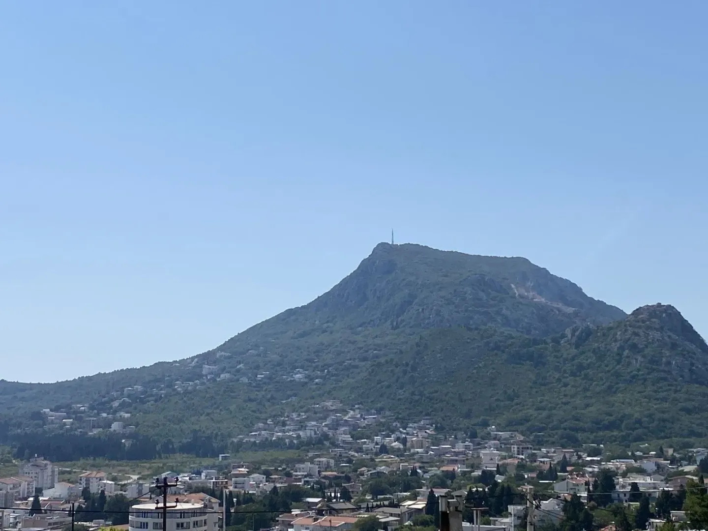 Pogled na planinu i naselje pod vedrim nebom.