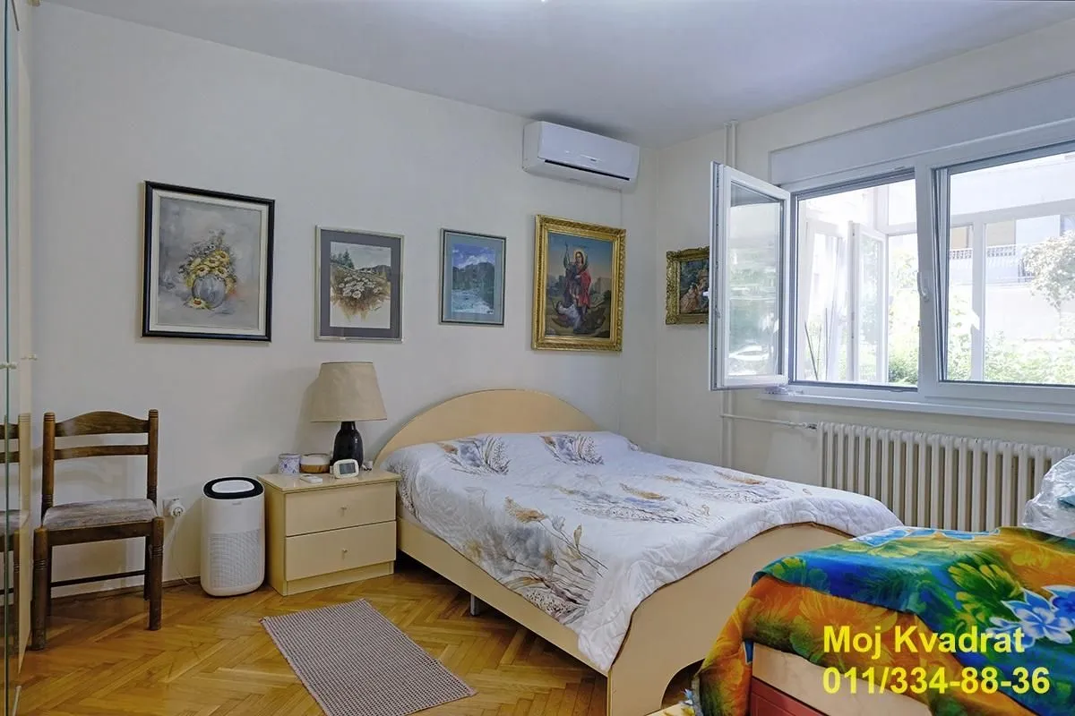 Nameštena spavaća soba sa bračnim krevetom, noćnim stočićem i slikama na zidu.