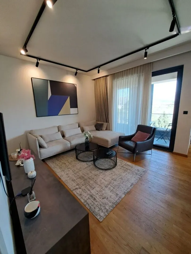 Dnevna soba sa ugaonom garniturom, foteljom i izlazom na terasu.