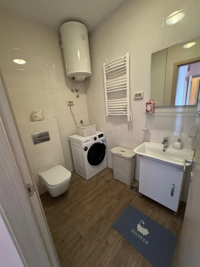 Manje kupatilo sa tuš kabinom, umivaonikom, WC šoljom i mašinom za veš.