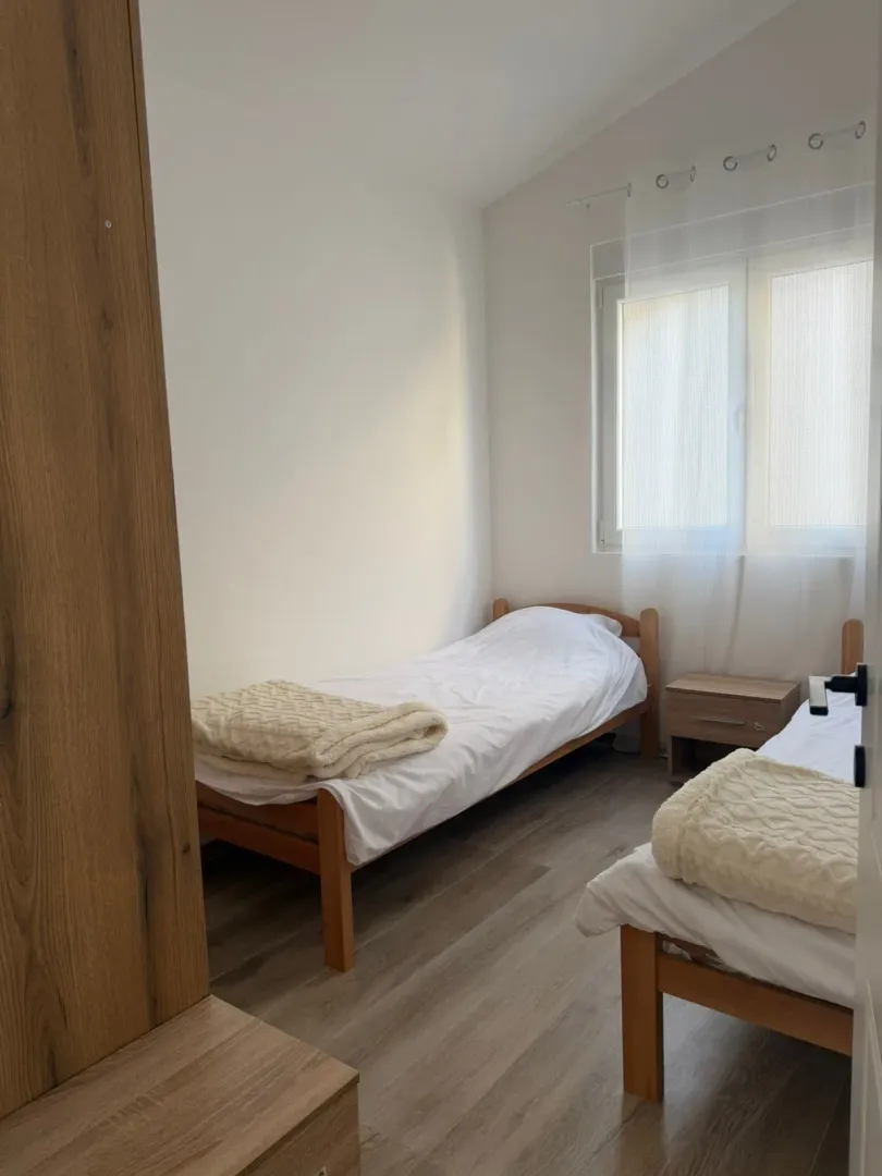 Manja spavaća soba sa dva drvena kreveta i prozorom.