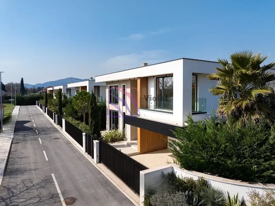 Pogled na spoljašnjost moderne vile sa uređenim dvorištem i ulicom ispred.