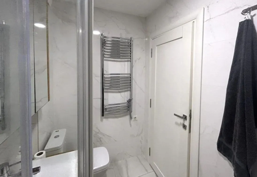 Modern bathroom with white tiles, shower cabin, and a white door.