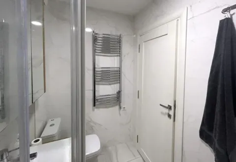 Modern bathroom with white tiles, shower cabin, and a white door. - image 6