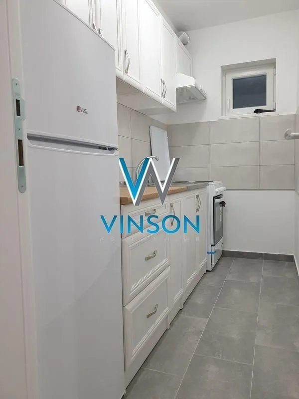 Manja bela kuhinja sa frižiderom i šporetom.