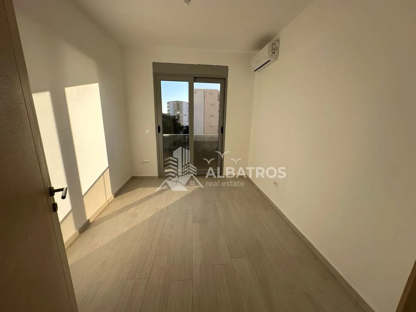 Prazna soba sa laminatom i izlazom na balkon.