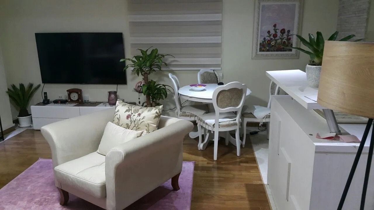 Dnevna soba sa garniturom, televizorom i trpezarijskim stolom.