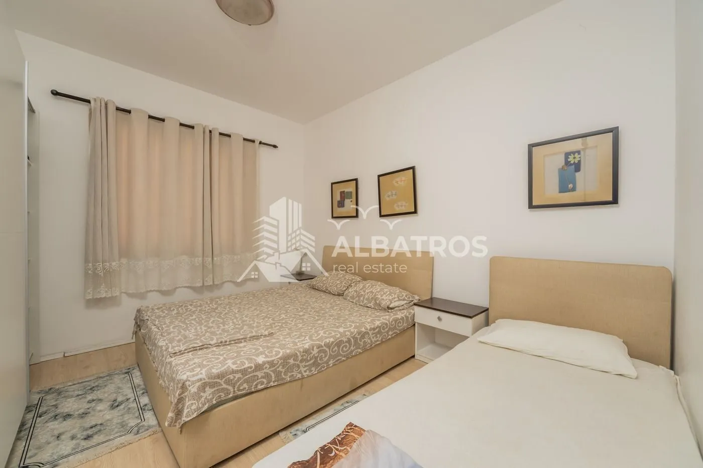 Bedroom with two beds, a window with curtains, and pictures on the wall.