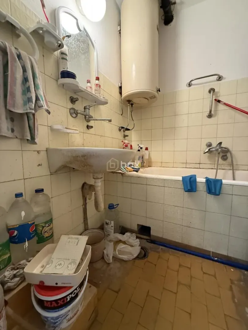Starije kupatilo sa kadom, umivaonikom i pločicama na zidovima.
