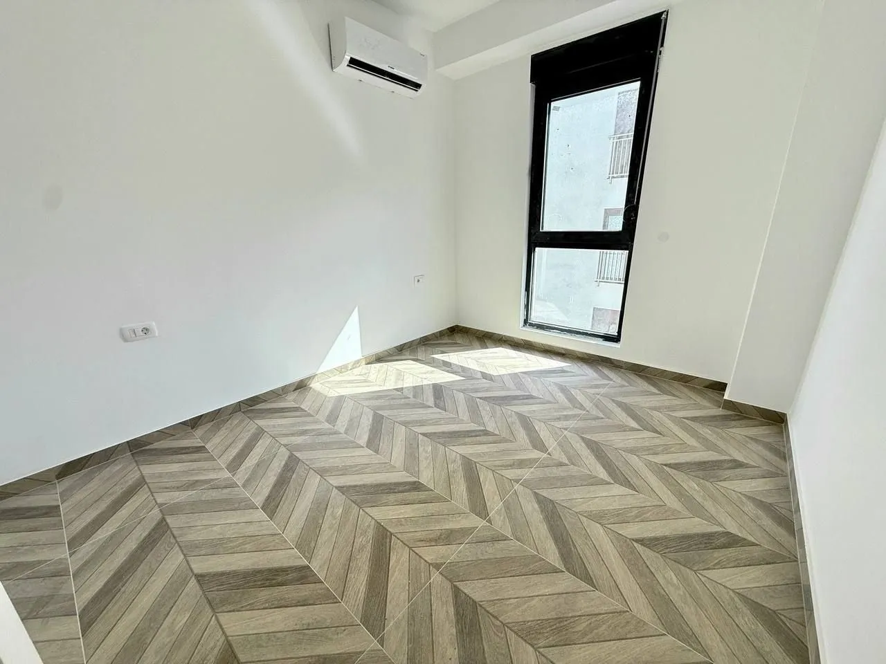 Empty room with light walls, wooden flooring, and an air conditioner.