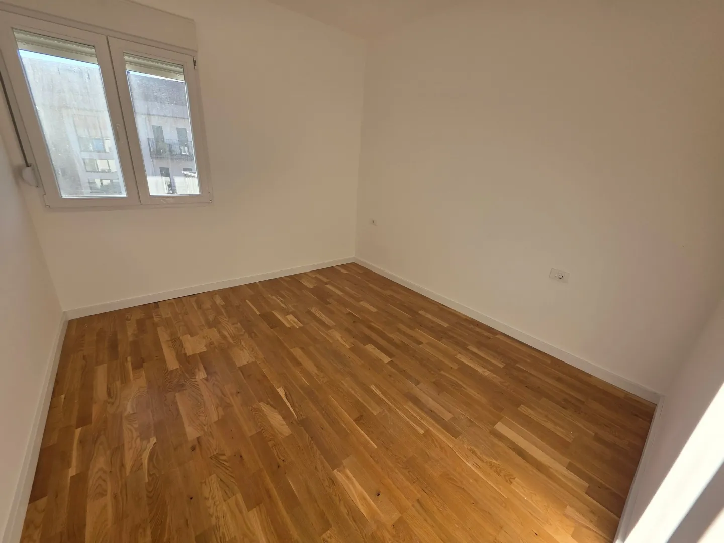 Prazna soba sa drvenim parketom i bijelim zidovima.