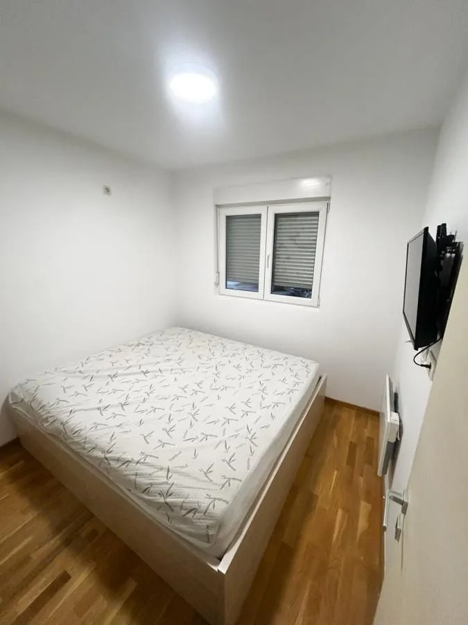 Manja spavaća soba sa bračnim krevetom, drvenim podom i televizorom na zidu.