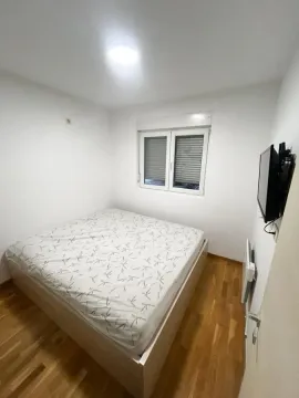 Manja spavaća soba sa bračnim krevetom, drvenim podom i televizorom na zidu. - image 5