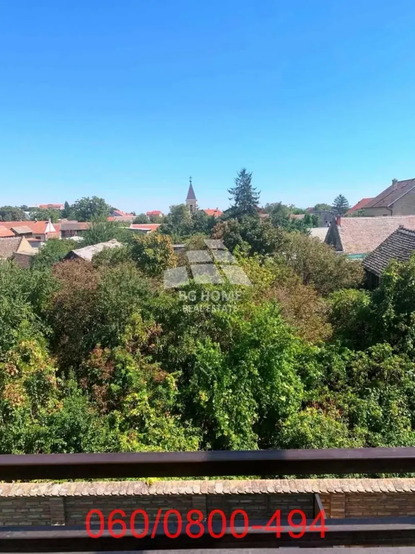 Pogled sa terase na naselje puno zelenila i krovove kuća.