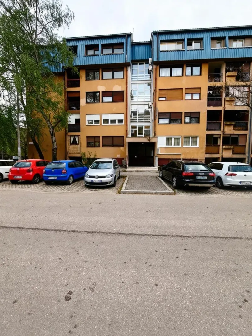 Eksterijer stambene zgrade sa parkingom i ulazom.