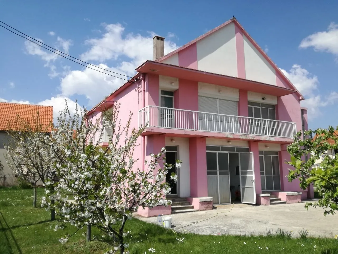 Dvospratna kuća roze boje sa dvorištem i procvjetalim drvetom.