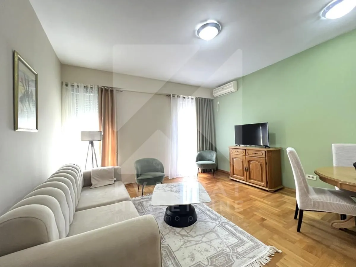 Dnevna soba sa garniturom, stočićem, televizorom i trpezarijskim stolom.