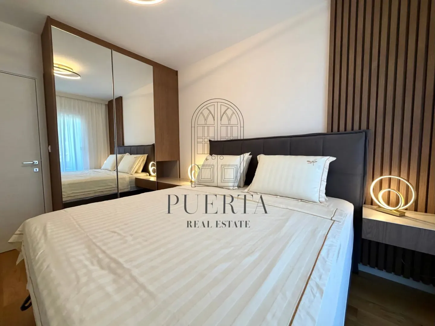 Modern bedroom with a double bed, mirrored wardrobe, and wooden wall panels.