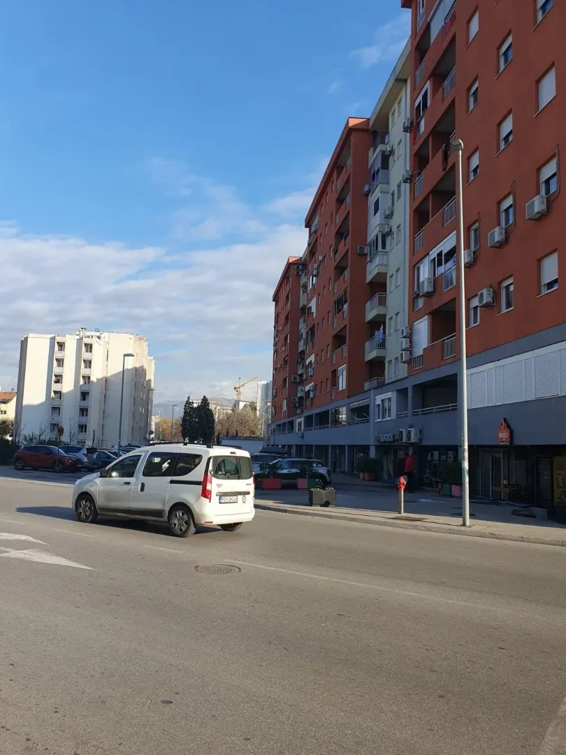 Vanjski izgled stambene zgrade pored ulice sa automobilom u pokretu.