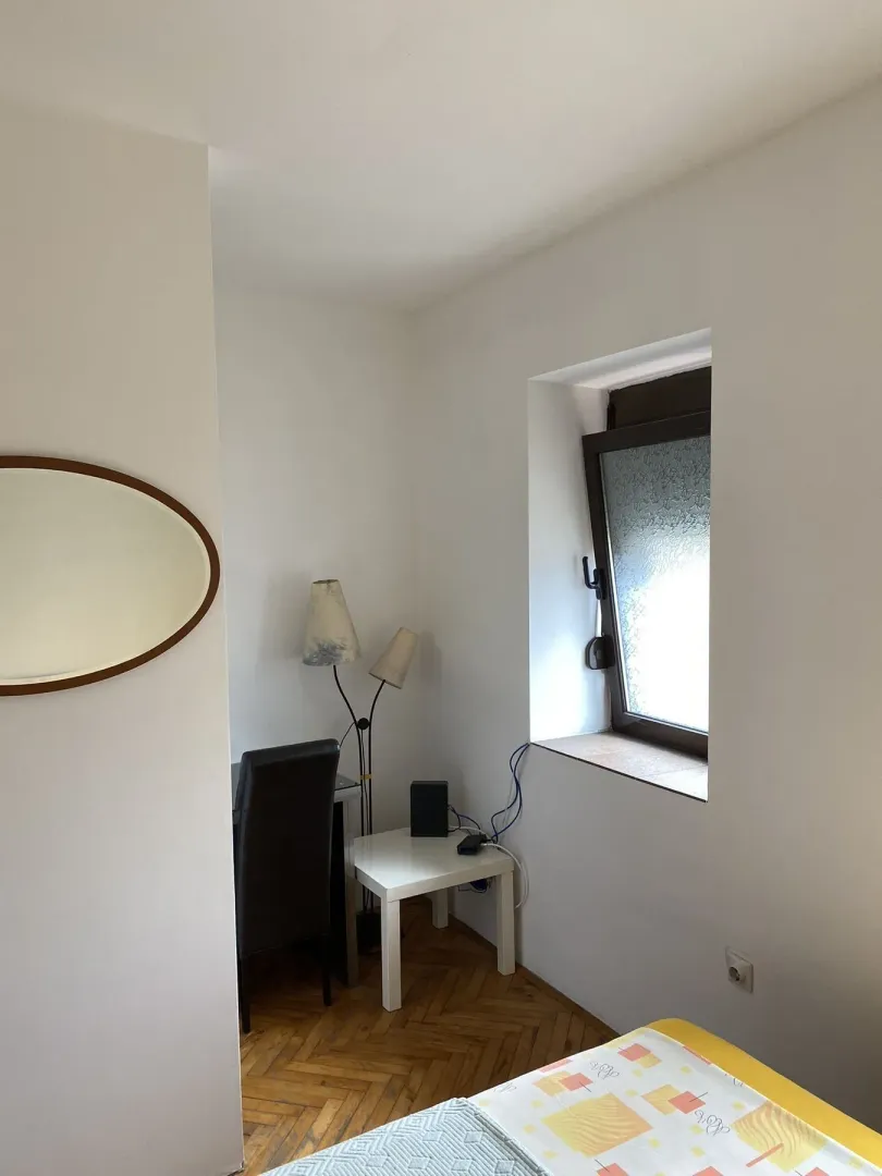 Dio spavaće sobe sa malim radnim stolom, prozorom i ogledalom na zidu.