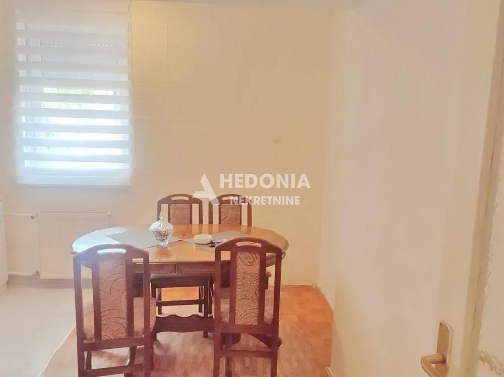 Trpezarija sa drvenim stolom i stolicama pored prozora.