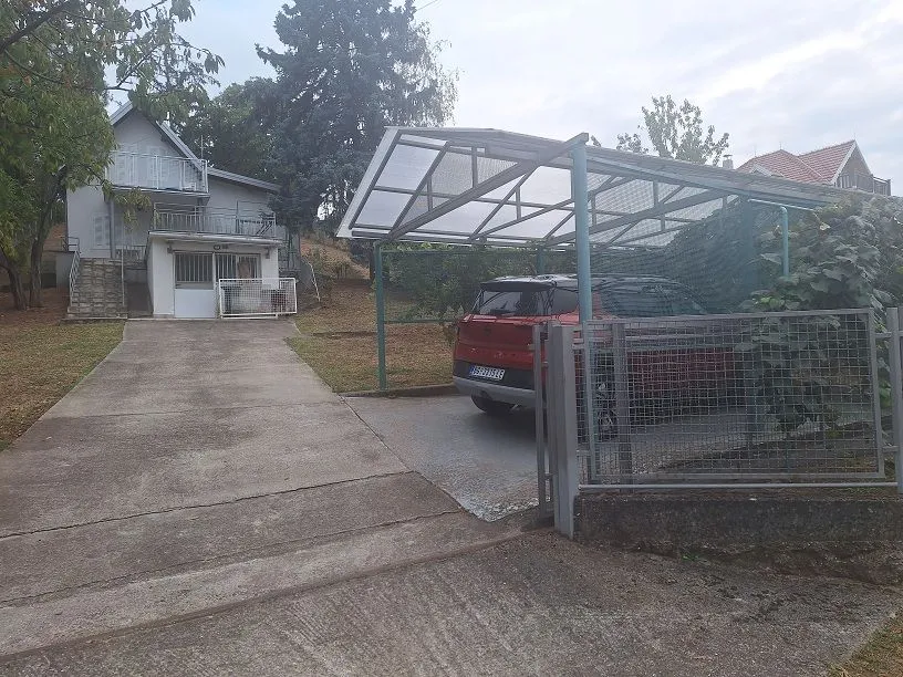 Dvorište kuće sa parkingom i nadstrešnicom za automobile.