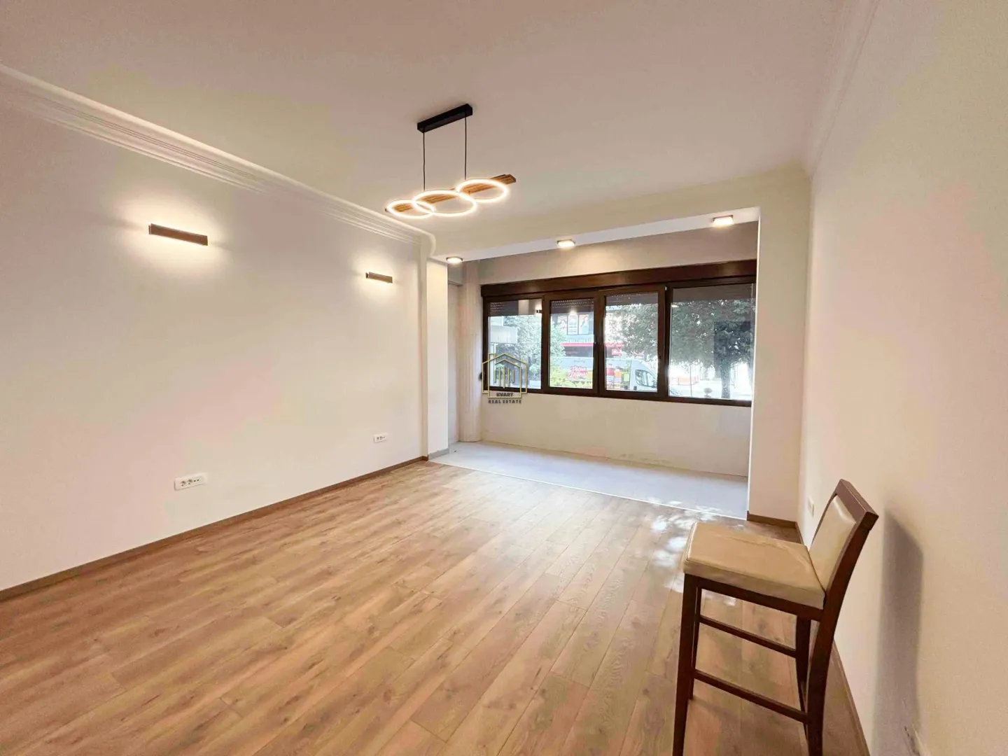 Empty living room with wooden flooring, modern lighting and large windows.