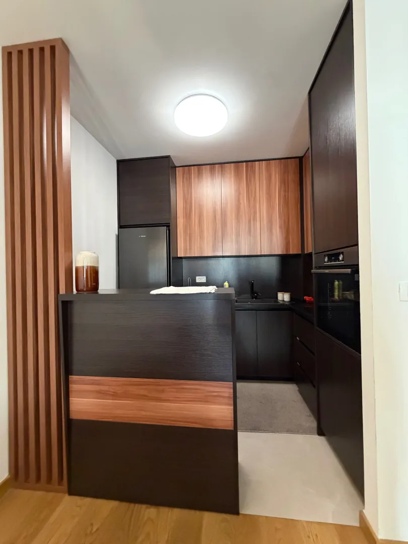Modern dark-toned kitchen with wooden elements and an integrated refrigerator.