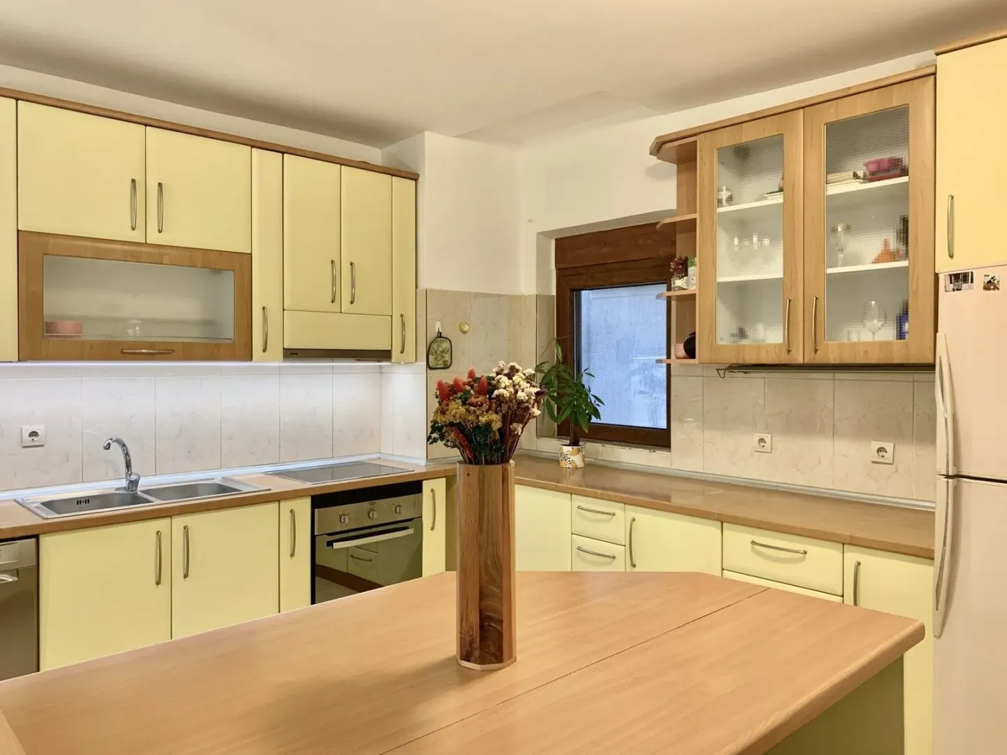 Bright kitchen with light yellow cabinets, wooden countertops, and a kitchen table.