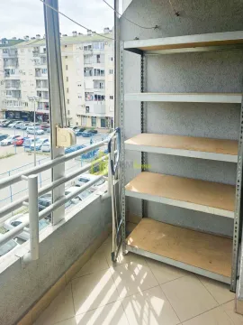 Enclosed balcony with a metal shelving unit and a view of the parking area and neighborhood. - image 11