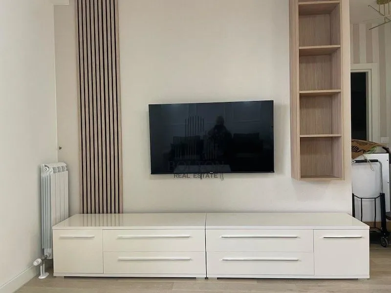 Dnevna soba sa TV-om, niskom komodom i zidnim panelom.
