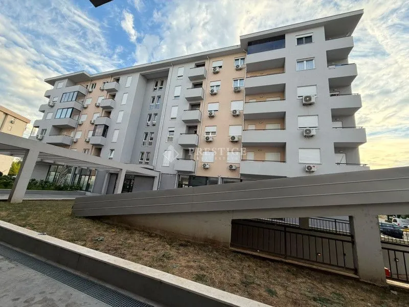 Spoljašnji izgled moderne stambene zgrade sa balkonom i uređenim dvorištem.
