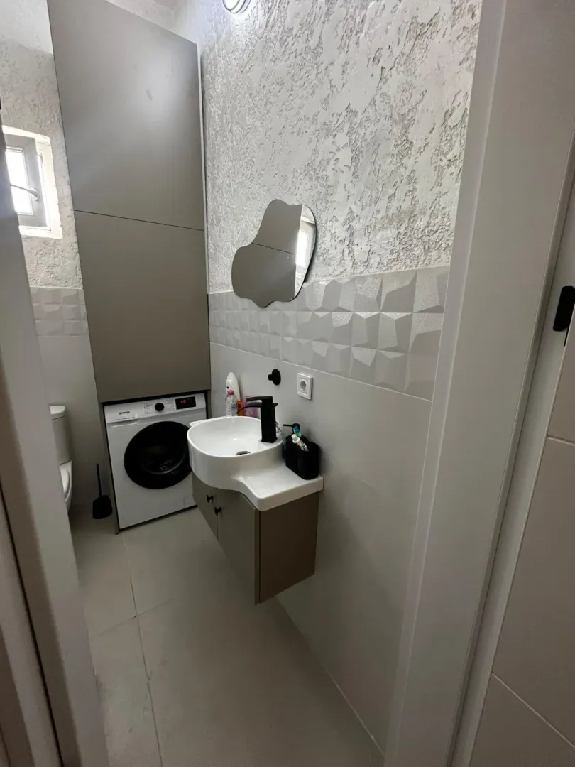 Manje kupatilo sa umivaonikom, ormarićem, ogledalom i mašinom za veš.