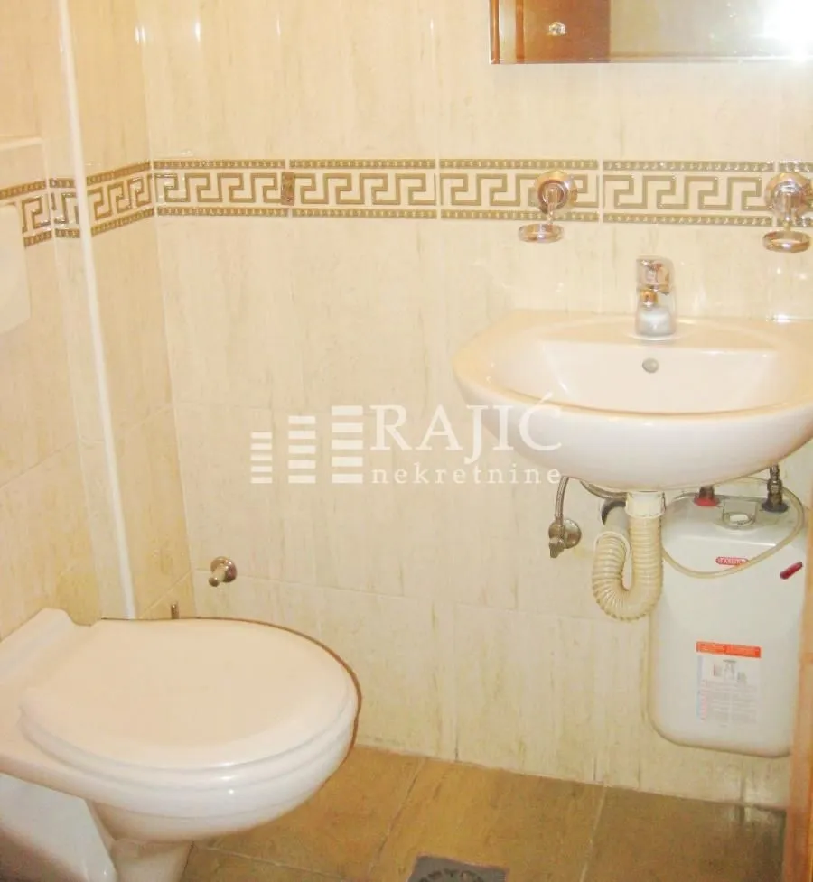 Smaller bathroom with a washbasin, toilet, and water heater.