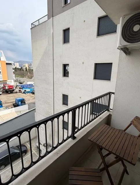 Manji namješteni balkon sa drvenim stolom i stolicama i pogledom na okolne zgrade.
