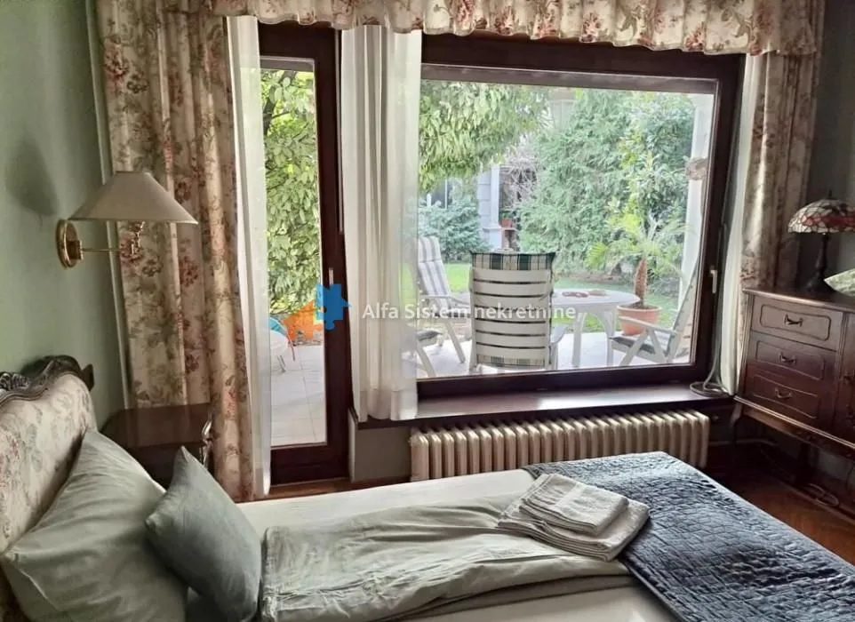 A bedroom with a bed and a large window overlooking the yard.